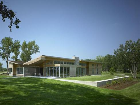 The butterfly roof satisfies the subdivision's minimum-slope requirement, though perhaps not in the way the document's drafters anticipated. A level section of yard retained by a low concrete wall serves as a green deck.