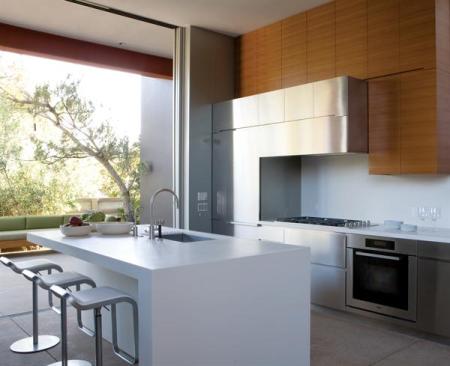 Stainless steel cabinets form a unified front with the stainless appliances. Teak cabinets above inject a note of warmth. The island picks up on the wall assembly's nested "L" shapes and Corian counter