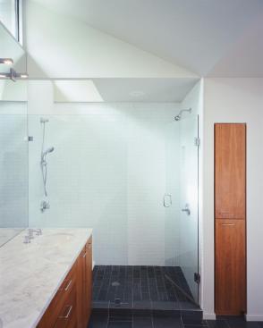 A seamless mirror reaches from vanity up to clerestory windows and spans from shower to tub (right). The oversized reflection helps enlarge the small bath. In lieu of a medicine cabinet, a narrow cabinet to the side of the shower holds pills and potions.