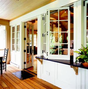 Bifold windows divide the kitchen from the screened-in porch, while glass upper cabinets act as a conduit for sunlight.