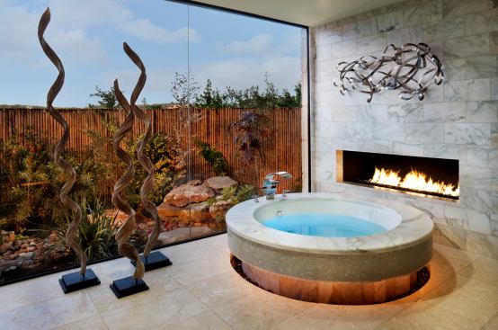In this marble master bath, the round Jacuzzi-style tub has a view of the bamboo garden and a fireplace close at hand. Architect: Susan Jauregui; Builder: Jauregui Architecture Interiors Construction