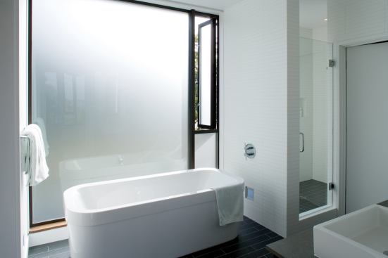 The freestanding tub occupies a niche backed by a wall of etched glass, which provides ample daylight without compromising privacy.