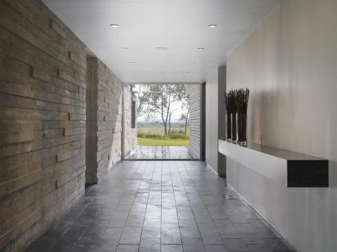 The long concrete wall borders the gallery-like entrance hall, and the fountain pool that lies beyond its glass end wall.