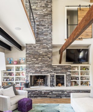 The living area’s two-story, stone-clad fireplace and built-in bookshelves add a sense of warmth to the industrial modern-themed space.