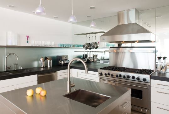 English feared the mirrored wall would collect water splashes if continued behind the sink. So he sandblasted it and tucked it under a long stainless steel shelf. It reflects light back onto the black granite and contributes a feeling of greater depth to 