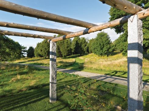 Rustic and refined materials merge in the Longmeadow kitchen garden, where a vine trellis of rough-hewn beams is strung with stainless steel cables between granite columns.