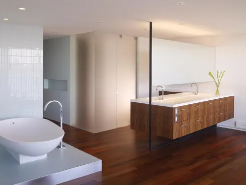 A two-sided peninsula emerges from the west wall, its mirror and its floating, figured-walnut cabinet supported by a slender, straplike column of gun-blue steel.