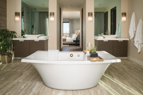 Spa Inspired With sedate, neutral-colored walls and vanities and warm wood-look travertine flooring, the 437-square-foot master bathroom provides a serene escape. Kohler products rule the day: Leaf vessel sinks, brushed bronze fixtures, San Souci touchless toilet, and the main attraction, an Escale BubbleMassage freestanding tub. His-and-hers TVs are installed behind the mirrors.