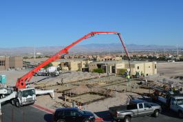 A pump truck flows concrete to the back of the house for deepened footings near the pool.